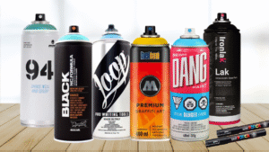 Colorful spray paint cans from top graffiti brands like Montana, Molotow, Loop, Kobra, and Ironlak arranged artistically on a graffiti-covered wall.