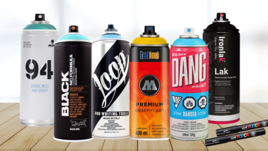 Colorful spray paint cans from top graffiti brands like Montana, Molotow, Loop, Kobra, and Ironlak arranged artistically on a graffiti-covered wall.